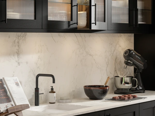 Modern kitchen interior with white marble countertop and backsplash, black matte faucet, dark bowl, stand mixer, recipe card holder, and black cabinetry with frosted glass upper doors showing kitchen items inside